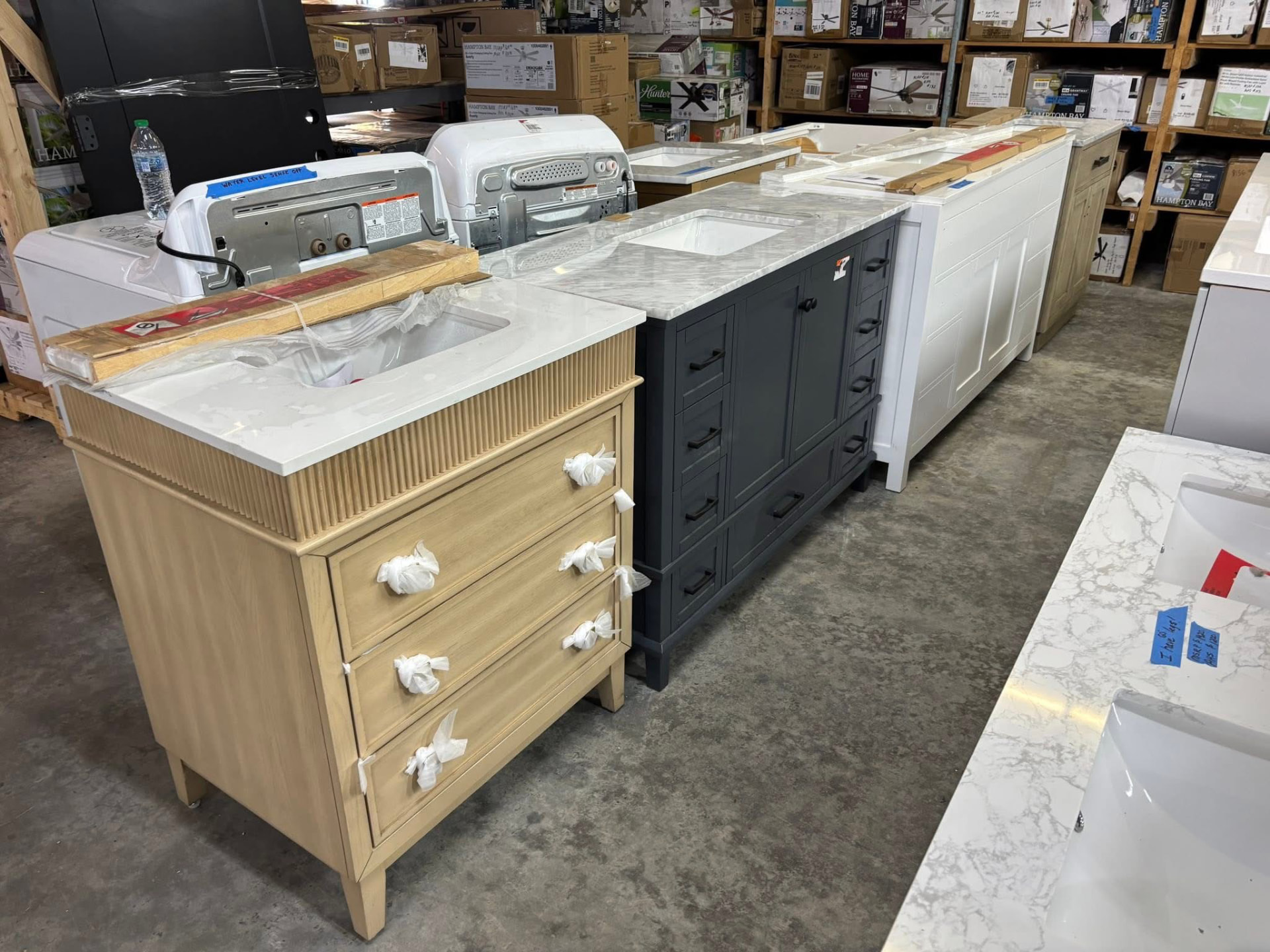 Row of new bathroom vanities in natural wood, navy and white finishes with marble and quartz tops at Austin's Home Supply & More