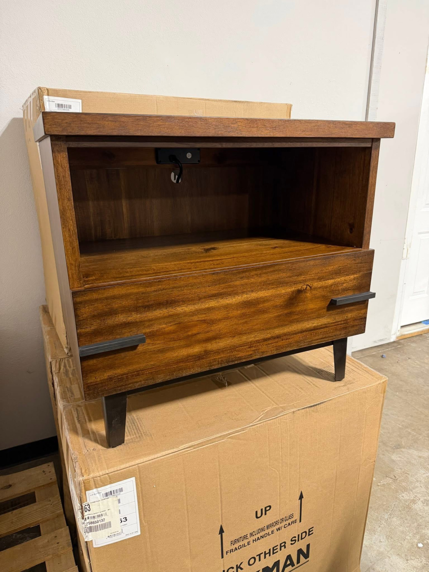 New solid wood nightstand with a black metal base sitting on its unopened carton