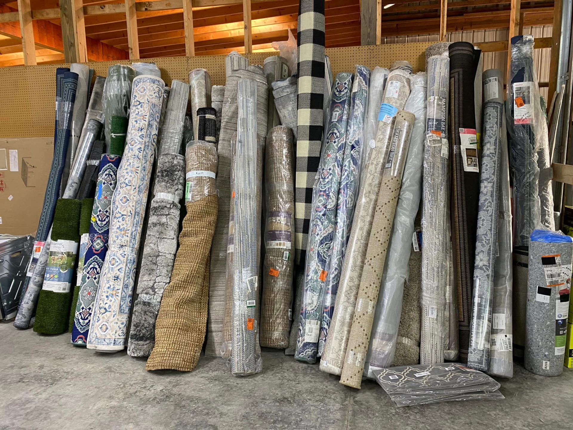 Dozens of rolled area rugs and runners standing against the wall inside the warehouse